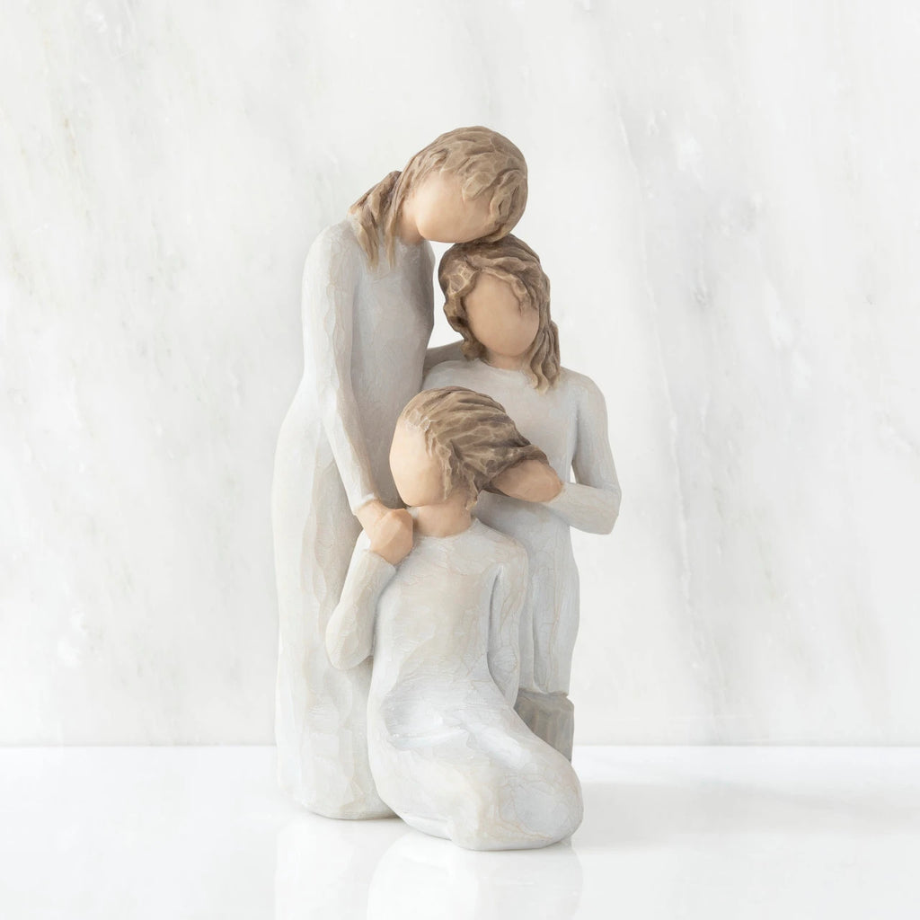 Front view, figurine of three females in cream dresses: one standing with arm around kneeling female, and holding hand of seated female