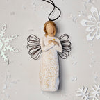 Willow Tree Remembrance Ornament, 4.5”h hand-painted resin angel figure in cream dress carved with symbols of nature, wire wings, crossed hands under small gold-leaf heart, brown elastic cord, laying amongst snowflakes