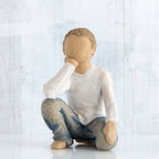 Small faceless boy figurine sitting with elbow on knee - wearing white shirt and blue jeans
