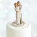 Willow Tree Together Cake Topper, 6”h hand-painted resin figure of couple, standing with arms around each other, dressed in neutral colors, affixed to 3.5" diameter food-safe base of carved white flowers
