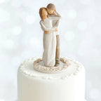 Willow Tree Together Cake Topper, 6”h hand-painted resin figure of couple, standing with arms around each other, dressed in neutral colors, affixed to 3.5" diameter food-safe base of carved white flowers