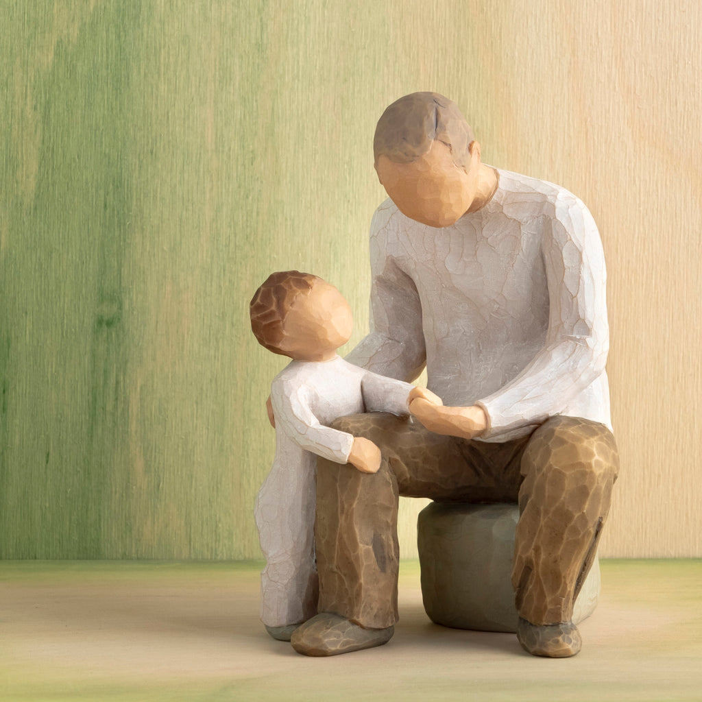 Willow Tree Grandfather, 6”h hand-painted resin figure of seated older man with toddler by his side, both dressed in neutral colors, in front of a green painting