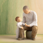 Willow Tree Grandfather, 6”h hand-painted resin figure of seated older man with toddler by his side, both dressed in neutral colors, in front of a green painting