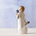 Small girl figurine wearing white dress holding two blue flower bouquets in each hand