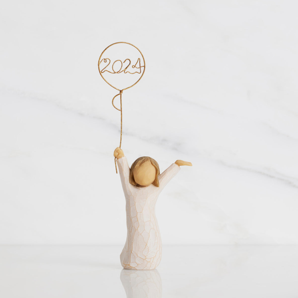 Front view: standing figure in cream dress, arms raised, holding gold wire balloon with 2024 written in gold wire inside