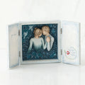 Open light wooden book with three parts - center is blue sky with two carved in faceless boy and girls hugging one another