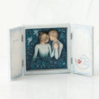 Open light wooden book with three parts - center is blue sky with two carved in faceless boy and girls hugging one another