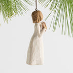 Side view female figure in cream dress, holding open book to her chest, ornament hook and loop attached to head