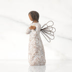Facing left: angel with wire wings, darker skin, arms crossed over gold heart, dress carved with symbols of remembrance