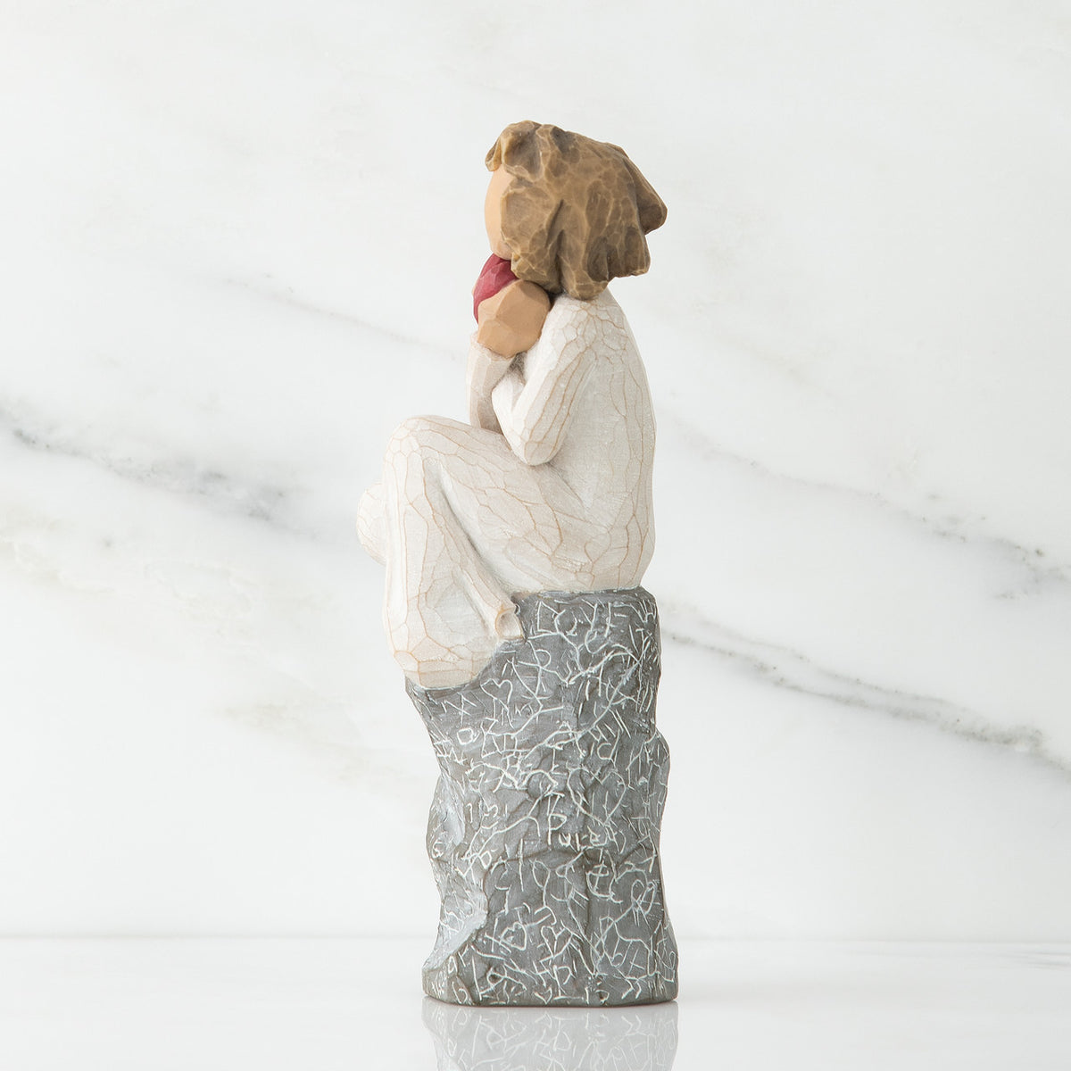 Side view of young girl in white sitting on grey rock with her hands up to her face