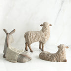 White donkey figurine laying down next to two white sheep figurines