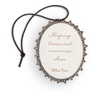 Back of small oval ornament with sentiment written in script on cream, edged in pierced-metal filigree