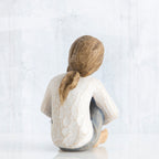 Back view of young brunette girl figurine in white shirt sitting down
