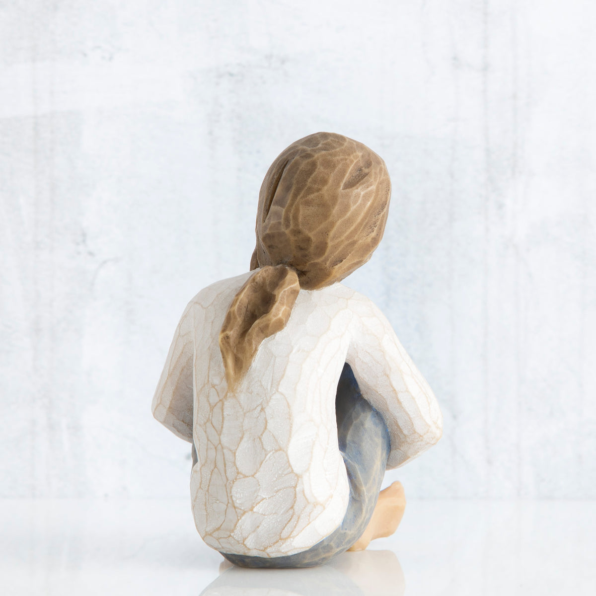 Back view of young brunette girl figurine in white shirt sitting down