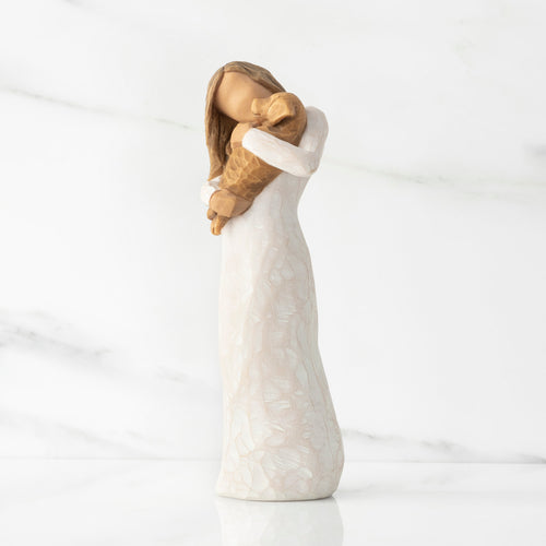 Left view, standing female figure in cream dress, holding golden color puppy in her arms