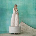 Willow Tree Close to Me Musical, 7.5”h hand-painted resin figure of woman embracing tween girl, both in cream dresses carved with intertwined vines and leaves, atop round, cream base containing musical element, in front of deep teal painting