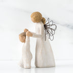 Side view of blonde angel figurine in white dress holding up baby figurine in white