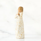 Gold haired woman in white/gold dress facing forward with arms to her chest