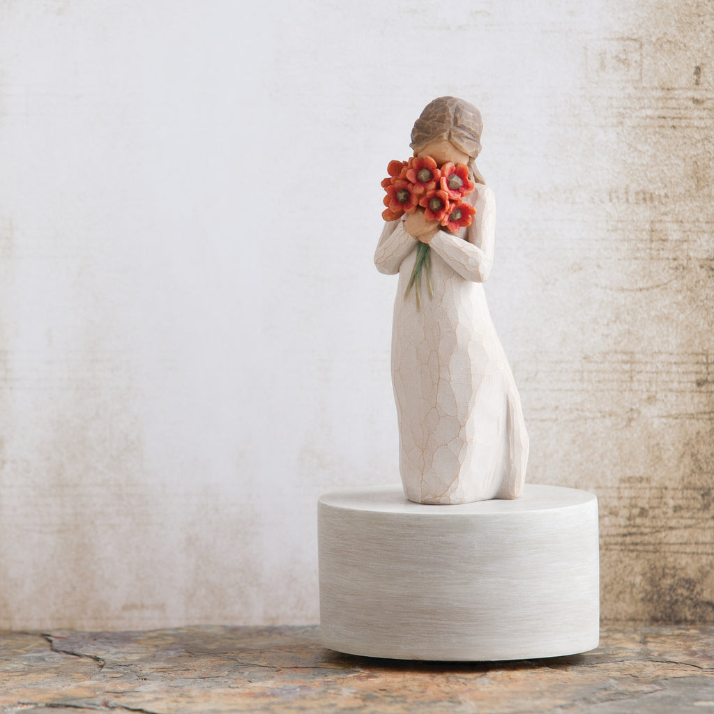 Willow Tree Surrounded by Love Musical, 7.5”h hand-painted resin figure in cream dress holding large bouquet of red-orange poppies up to face, atop round, cream base containing musical element, in front of cream painting