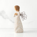 Left side view of standing female figure with wire wings in cream dress carved with natural symbols, hands crossed under gold heart on chest