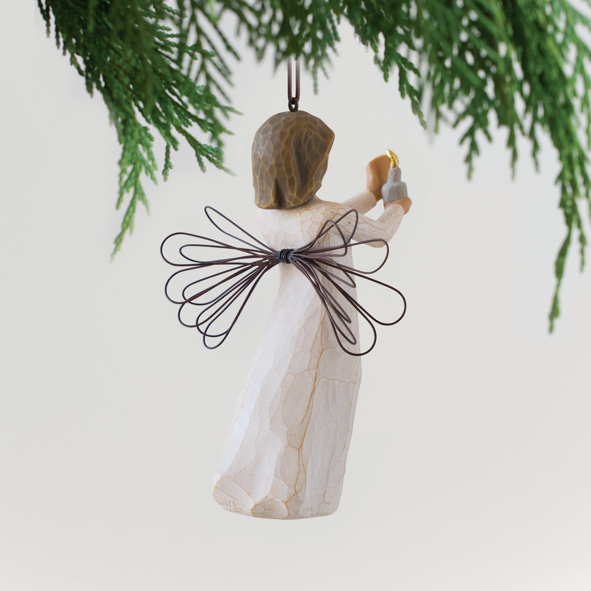 Back View: Figure with short brown hair wearing cream dress holding out a candle in her hands, ornament hook attached to head