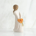 Back view of girl with brown hair in braid over right shoulder leaning forward as she holds orange flowers behind her back