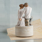 Man and woman figurine in white sitting holding hands on round large plaque and tan paper below it