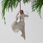 Back view of woman angel figurine ornament in white dress hanging from green tree