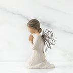 Side view of angel figurine in white kneeling holding her hands in prayer