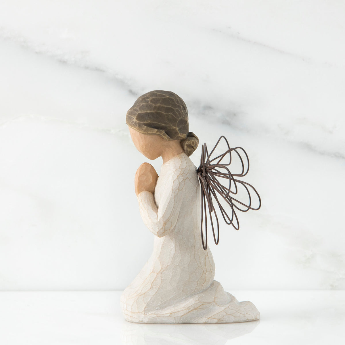 Side view of angel figurine in white kneeling holding her hands in prayer