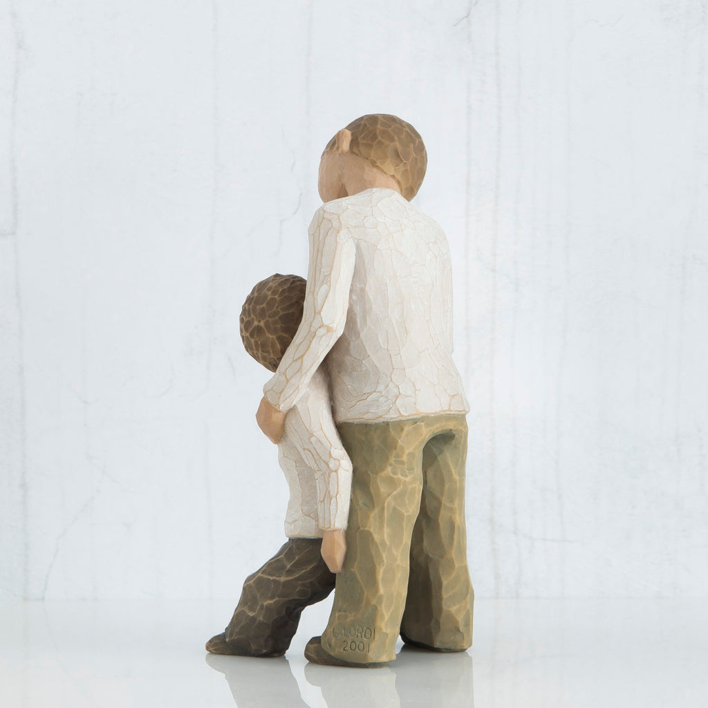 Two young boy figurines in white and brown pants facing the back hugging one another