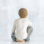 Back view of brunette boy figurine in white shirt and blue jeans sitting down