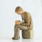 Side view of man figurine dressed in brown sitting on a rock holding baby figurine