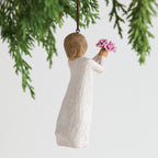 Back view of woman ornament with short brown hair, holding out a bouquet of pink flowers. Brown string attached to top of ornament