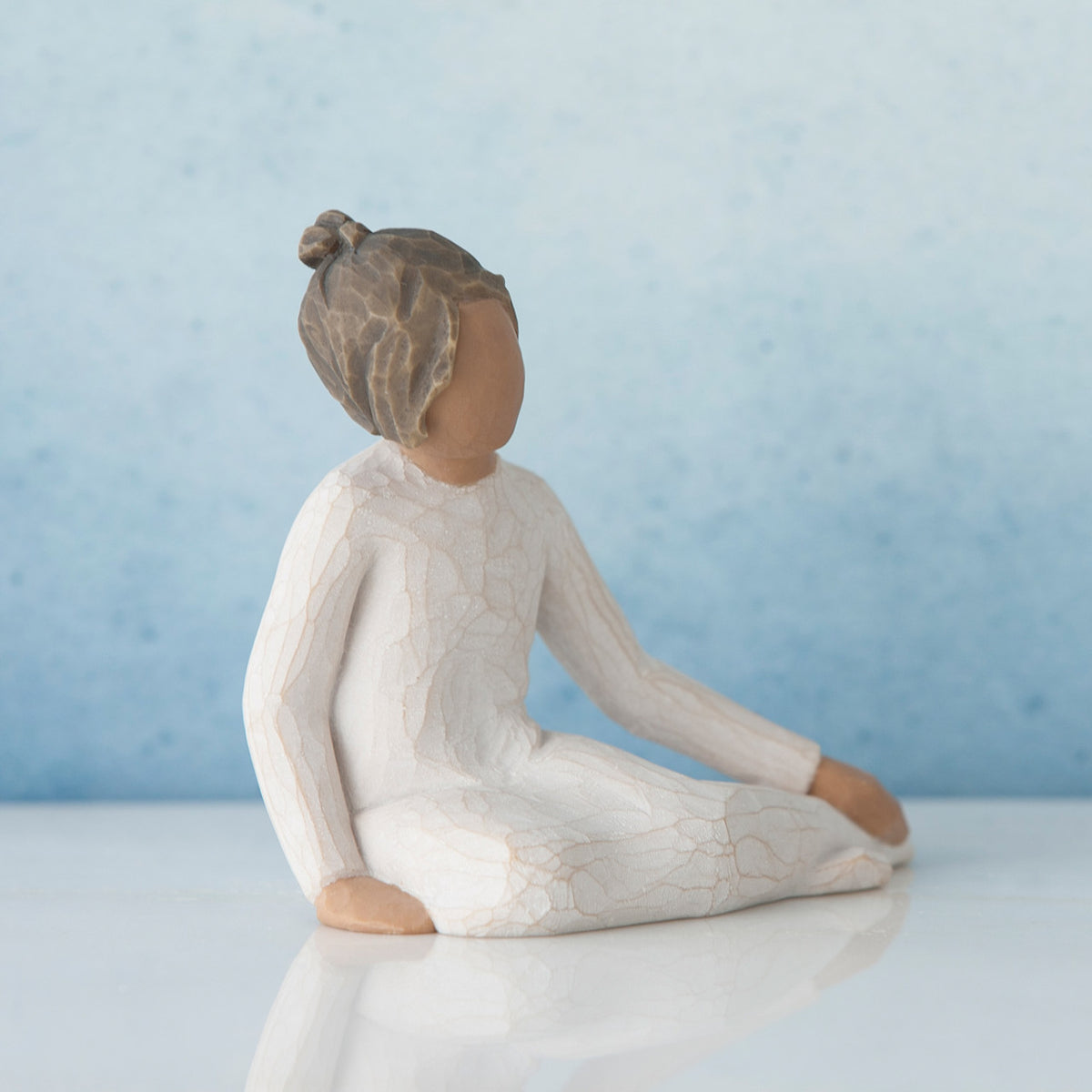 Small brunette girl figurine in white sitting down against blue background