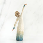 Girl figurine in white dress with blue bottom facing the back with her arms spread