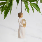 Facing right: Dated Ornament of figure holding pierced gold-leaf wreath of hearts. 2024 written on wreath; loop and hook in head