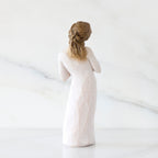 Back view: Standing figure in cream dress with hands to heart in empathetic gesture