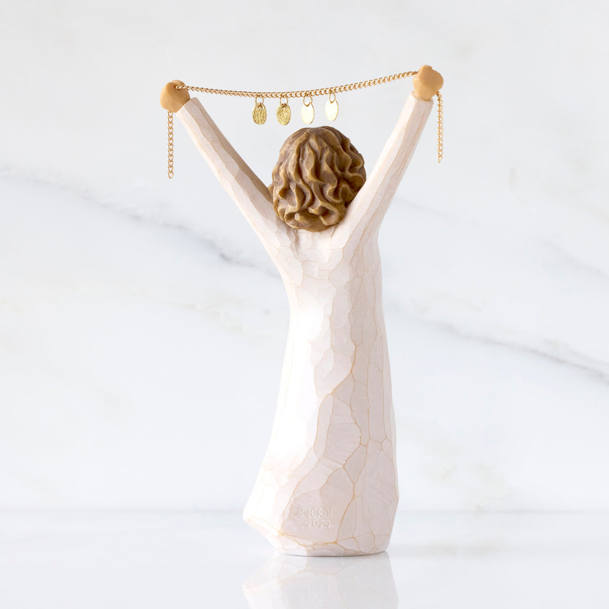 Willow Tree Courage 2025, back view of 6”h hand-painted standing figure in cream dress holding aloft a gold chain with 2025 etched on gold medallions