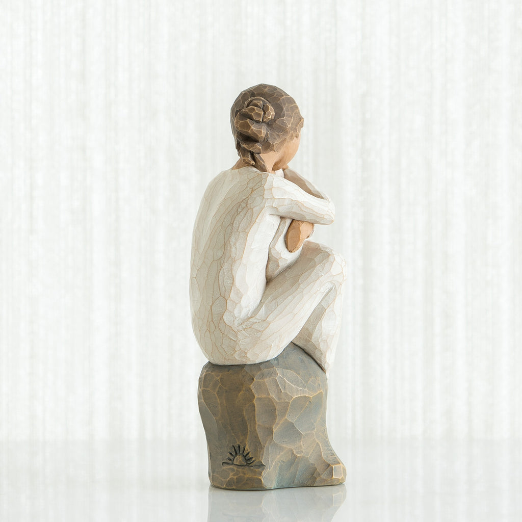 Back view of brunette girl figurine sitting down in white dress on rock