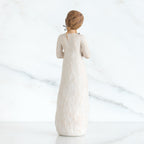 Back view of girl with brown hair in a bun holding three flowers with long stems up to her chest with both hands