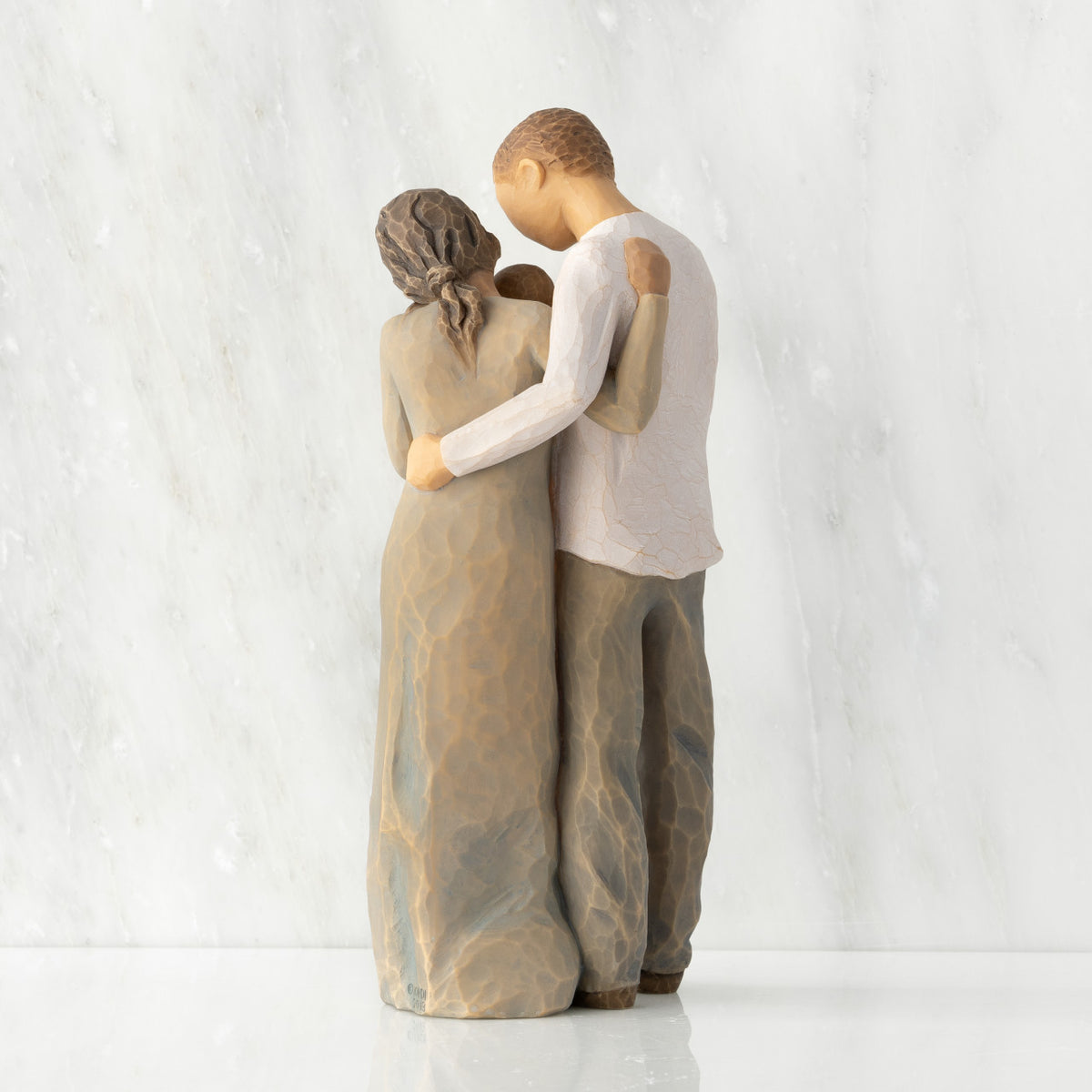 Back view of standing couple, woman has darker skin and hair; man has lighter skin and hair, holding a baby between them.