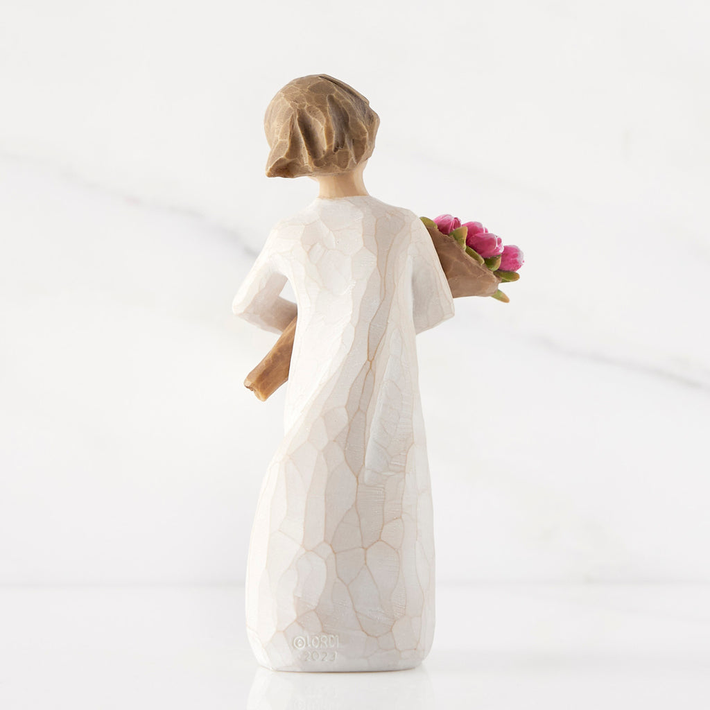 Back view of standing figure in cream dress holding bouquet of pink tulips