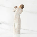 Back view, standing female figure in cream dress, holding dark color puppy in her arms