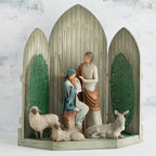 Light grey barn figurine with open doors, man and woman figurines in the center holding baby, two white sheep surrounding them