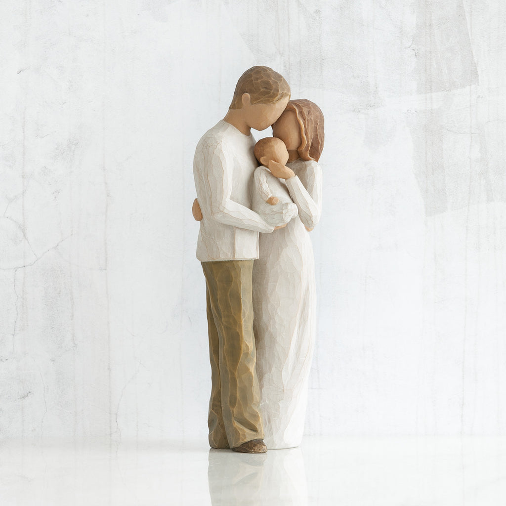 Man and woman figurines in white facing one another holding baby