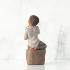 Back view: Figure of darker-skin child, kneeling on rock, holding wire circle with ‘love you’ written in wire