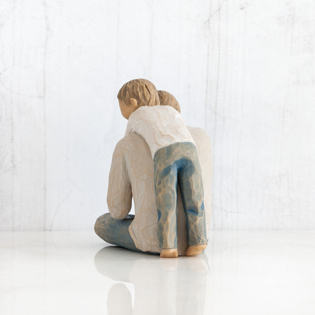 Back view of little boy figurine in blue jeans and white shirt hugging a larger father figurine