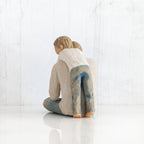 Back view of little boy figurine in blue jeans and white shirt hugging a larger father figurine