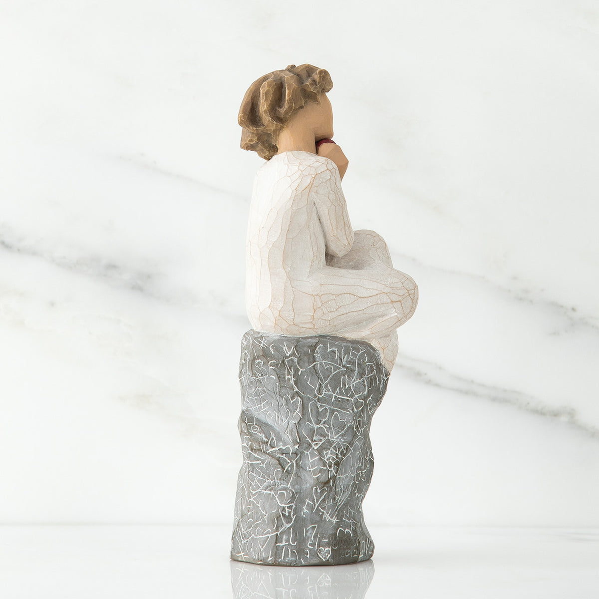Back view of brunette girl figurine in white dress sitting on grey rock